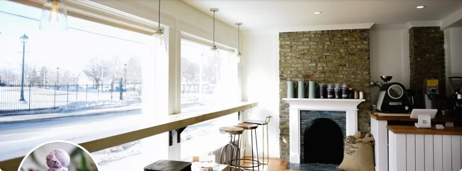 Inside The Parlour: a long wooden window bench with stools, a white fireplace with a brick wall, and the coffee bar