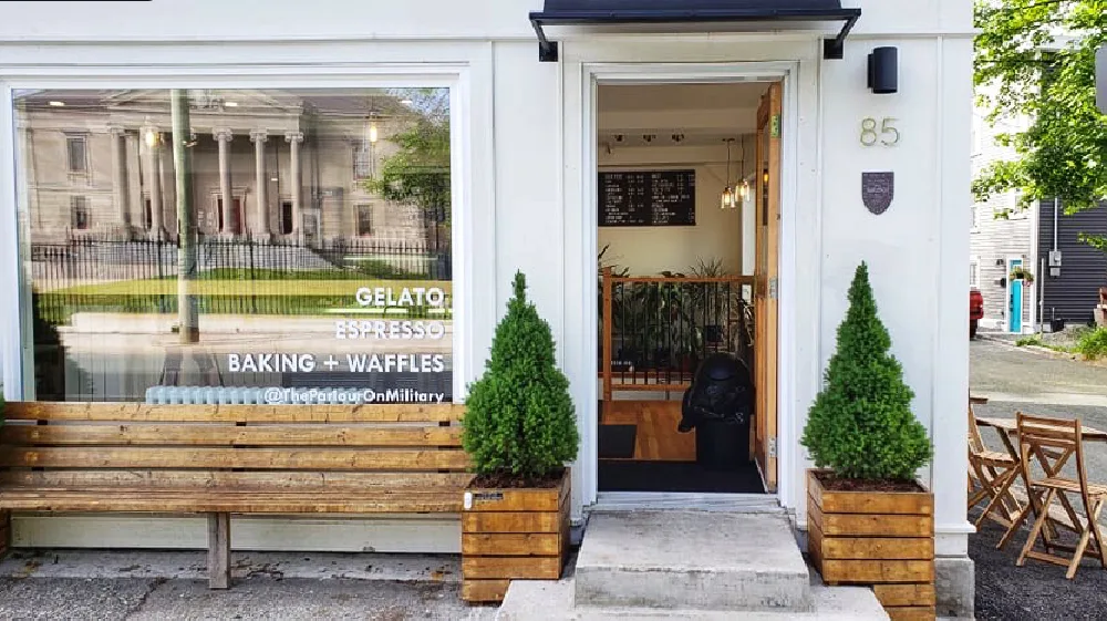 The white storefront of The Parlour at 85 Military Road with a wooden bench under the window and lettering reading gelato, espresso, baking and waffles